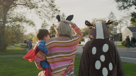 woman with two children in carnival costumes in honor of halloween. walking down the street of a small american town