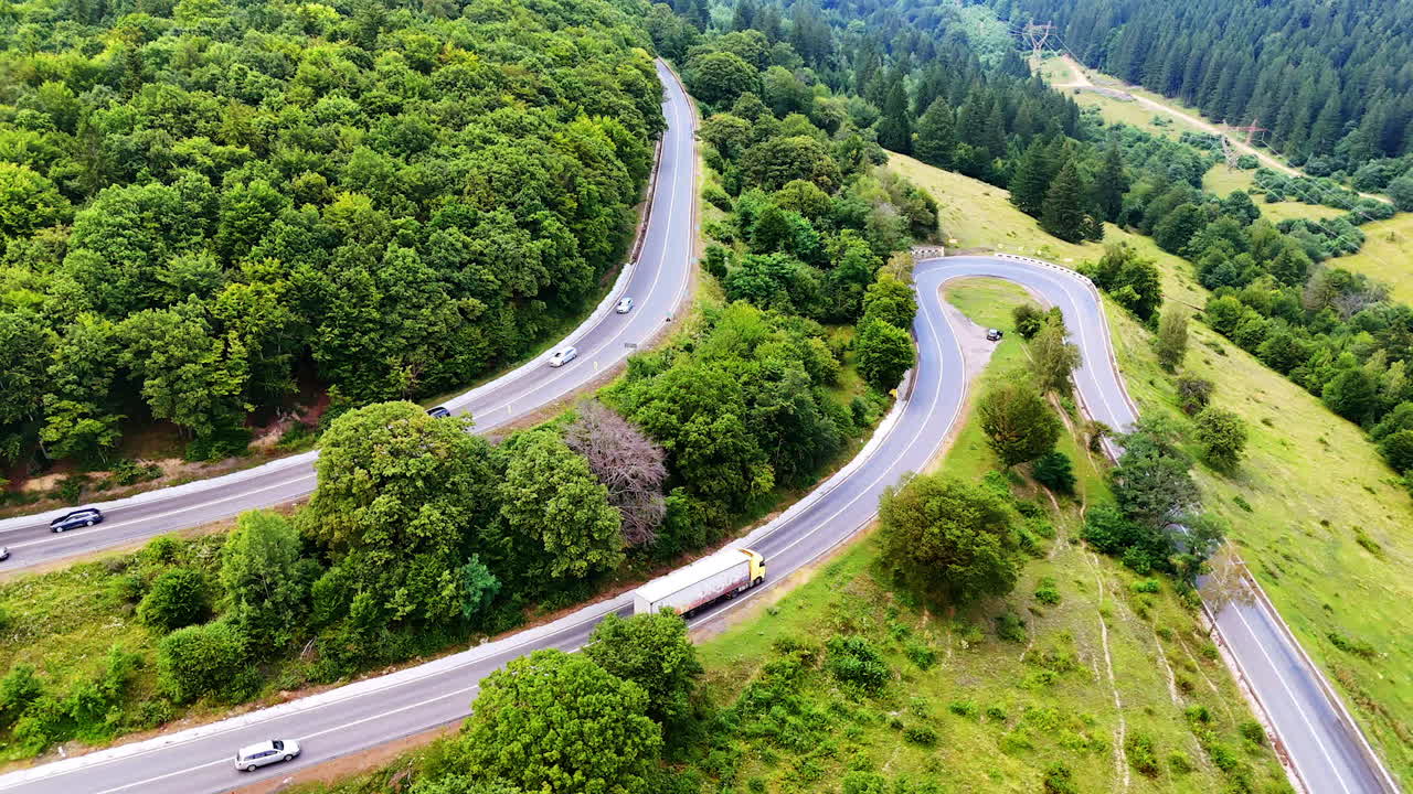 Twisting road in sunny woods. Cars navigate a winding road surrounded by lush green trees on a sunny day, highlighting the beauty of nature