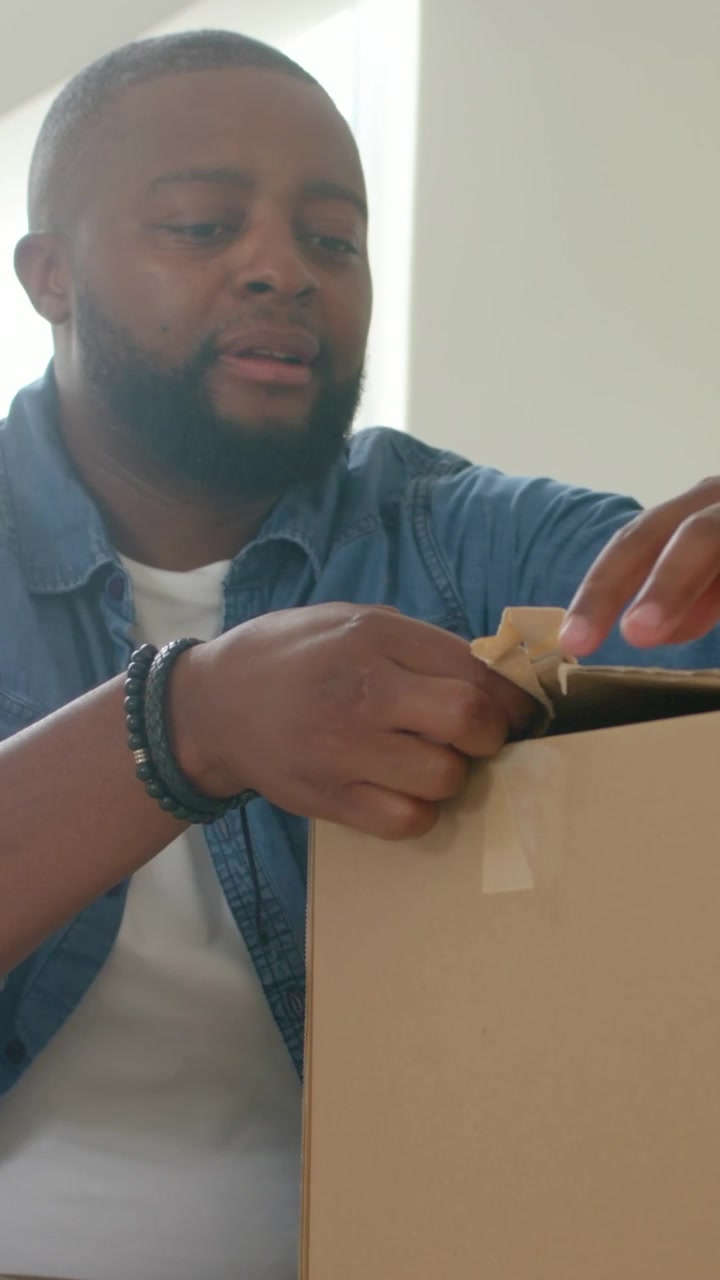 Vertical video: Lifting tape edge, man in denim peeling tape, checking box at home, copy space
