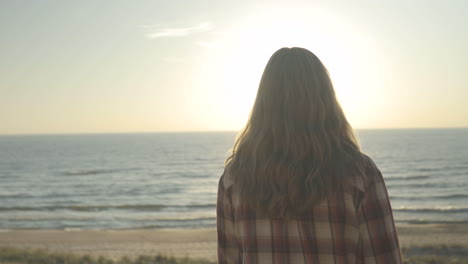 Handheld over the shoulder shot following a woman walking along the beach at sunset.  Shot in 4K