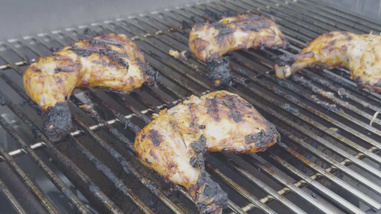 Grilled chicken legs cooking on stainless steel bbq grill. stainless steel tongs turn the charred chicken