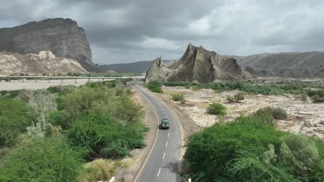 drone aéreo siguiendo el disparo sobre un coche que conduce a lo largo de la autopista rodeada de montañas en hingol, balochistan, pakistán en un día nublado