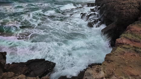 Las-Olas-Chocan-Con-Fuerza-Contra-Un-Acantilado,-Salpicando-Espuma-Blanca-Sobre-El-Borde-Rocoso,-Capturadas-En-Espectacular-Cámara-Lenta.