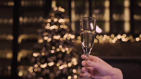 camera focuses on the hand of a woman holding a glass of champagne at the new year's party