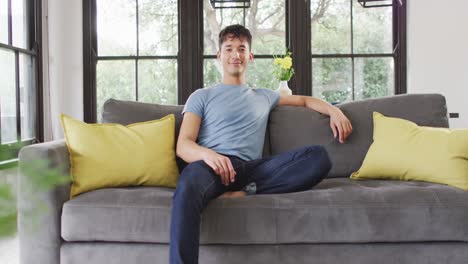 portrait of happy biracial man sitting on sofa, looking at camera and smiling