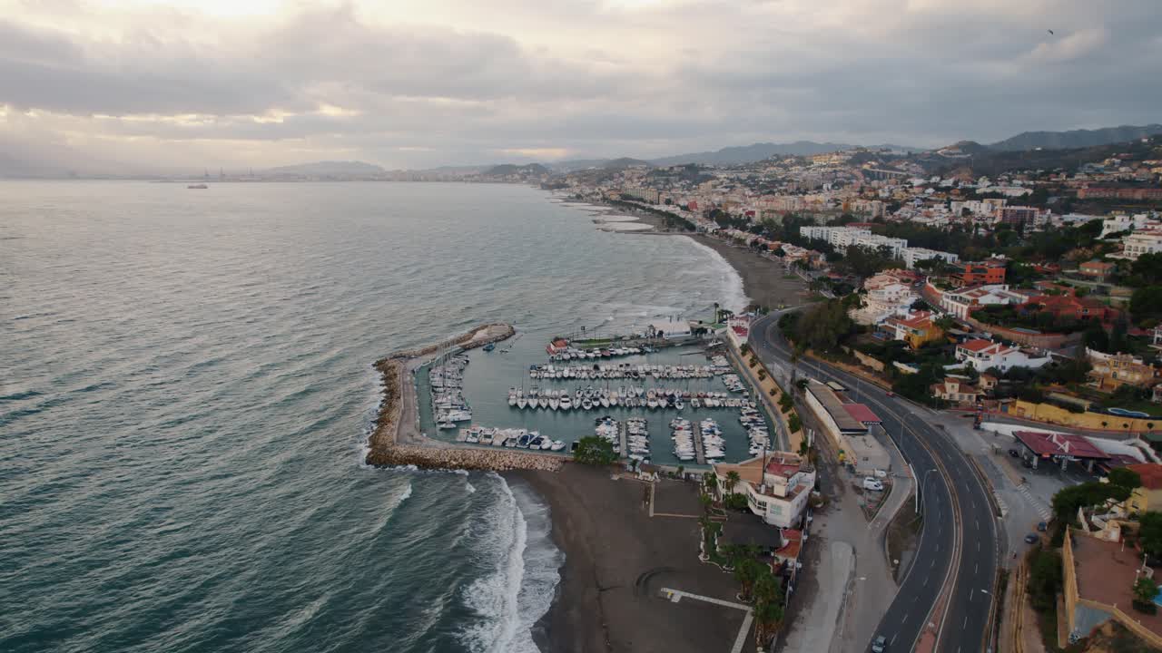 un dron aéreo en movimiento hacia adelante disparó sobre la playa de el candado y la carretera costera en málaga, españa, con vistas a la costa, al puerto deportivo y a las casas de playa.