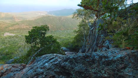 Reveal-of-hikers-climbing-down-rocks-with-green-mountain-landscape,-Curacao