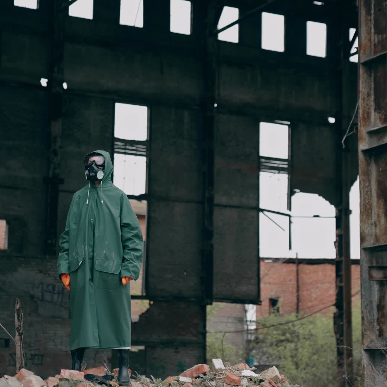 Ecologist in safety suit on ruined building background. Person in gas mask and protective clothes stands in dangerous place after chemical attack