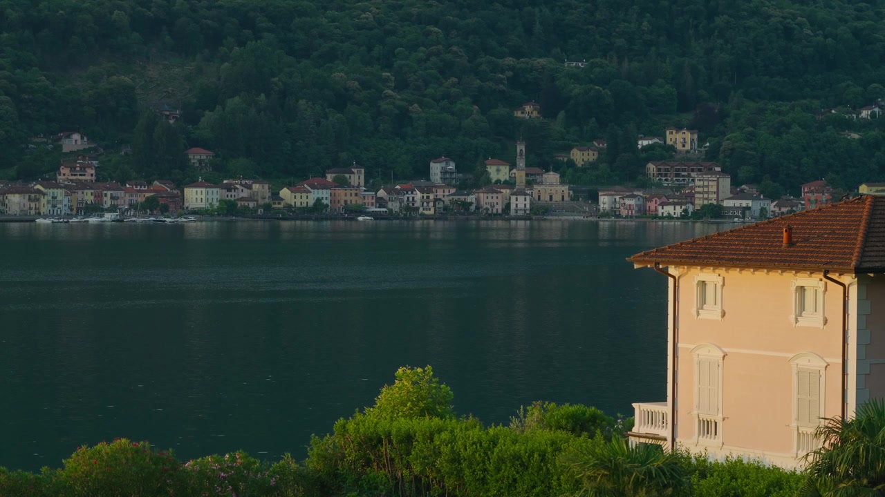 Vista panoramica di incantevoli case sul lago lungo il Lago di Lugano con acqua blu calma, rigogliose colline verdi e un'atmosfera pacifica, che mostra la bellezza del nord Italia