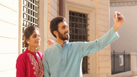 encantadora pareja india posando, sonriendo y tomando selfies con un teléfono inteligente