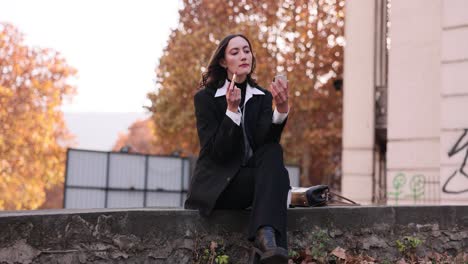 woman in a suit applying lipstick outdoors in autumn