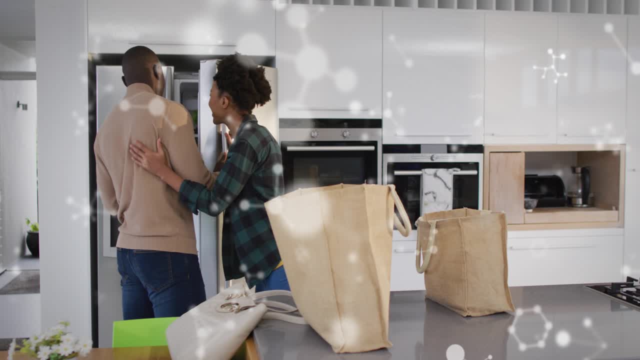 Man opening fridge in kitchen as woman embracing, activating health icons showing produce nutrients