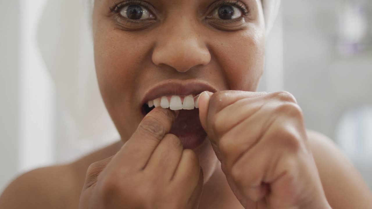 Happy african american woman flossing teeth and using smartphone in bathroom
