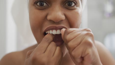 happy african american woman flossing teeth and using smartphone in bathroom