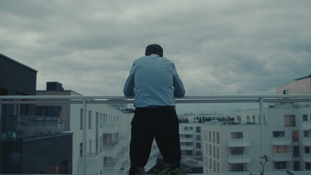 A sad man in a shirt smokes a cigarette on the balcony