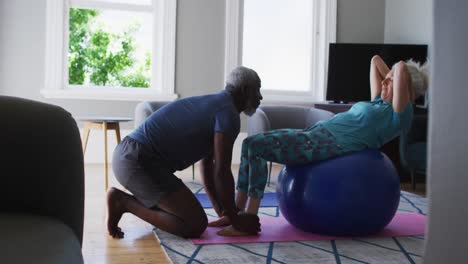 mixed race senior couple performing exercise together in the living room at home