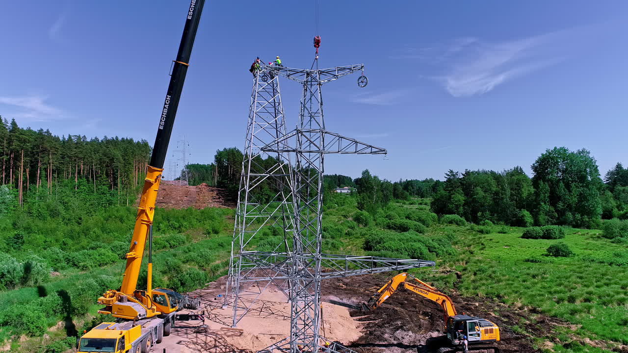 Electrical crew working on wires on a newly erected transmission tower pylon in the European countryside - aerial view