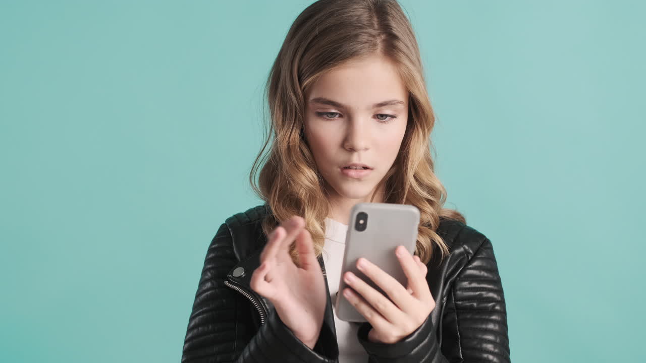 가죽 재을 입은 십대 백인 소녀가 스마트폰을 사용하고 미소 짓고 있습니다.