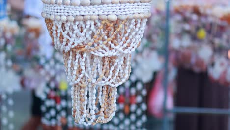 a hand gently touches a shell decoration in a vibrant phuket market, showcasing intricate craftsmanship and colorful surroundings