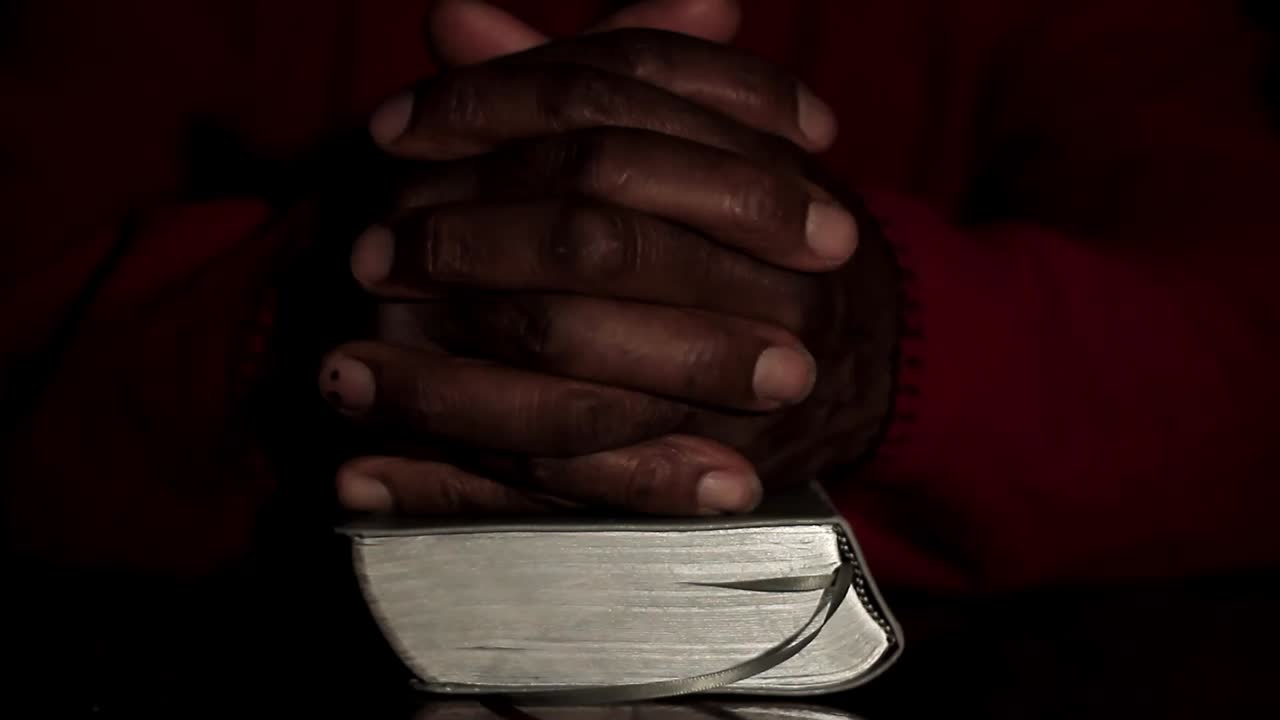 rezando a dios con las manos junto con la biblia y el hombre cruzado del caribe rezando con fondo negro almacen de video