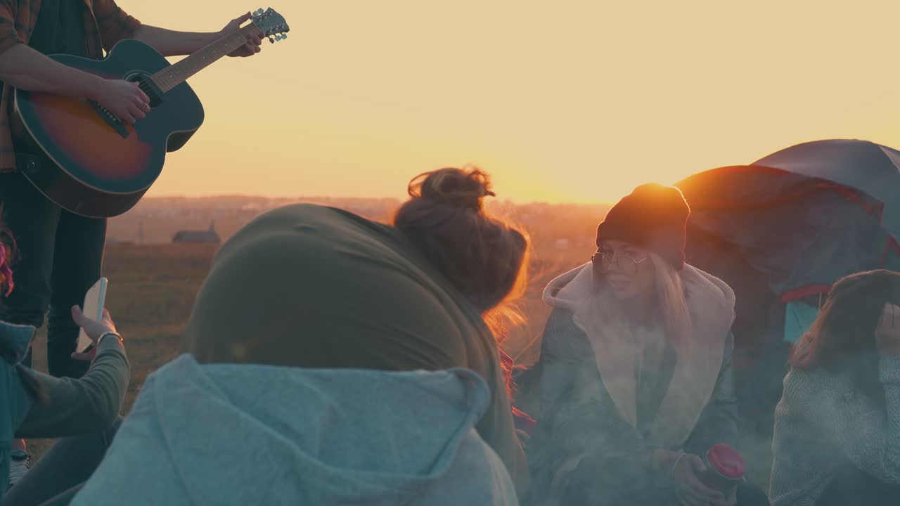 people rest listening to guitar by camp bonfire at sunset