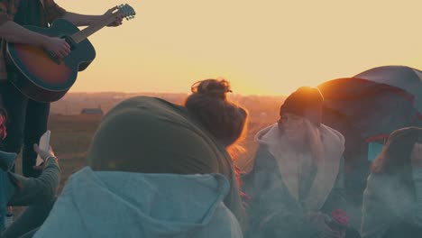 La-Gente-Descansa-Escuchando-La-Guitarra-Junto-A-La-Hoguera-Del-Campamento-Al-Atardecer.