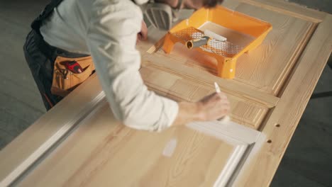 top view of a man in work uniform and respirators paints a wooden product with a brush in white