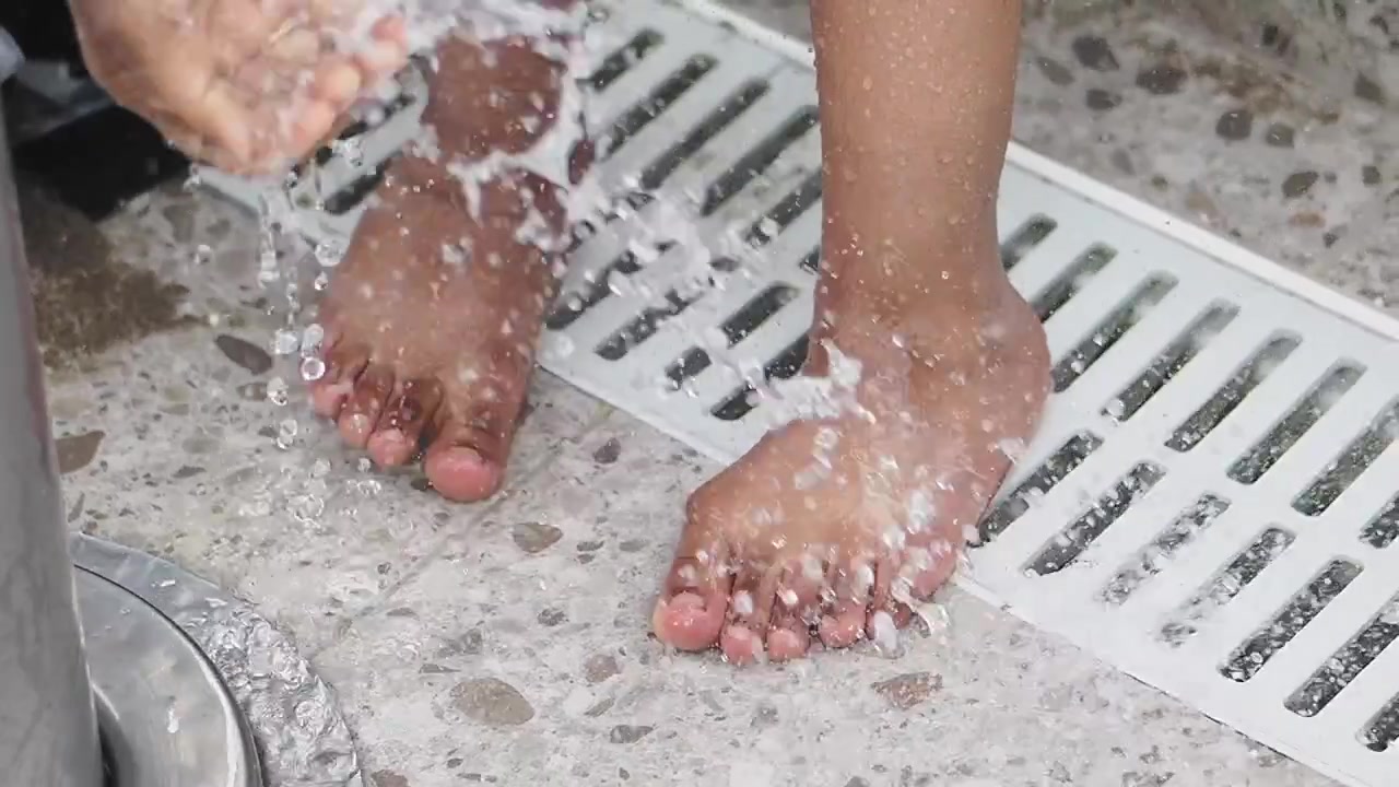 Persona enjuagándose los pies bajo una ducha exterior.