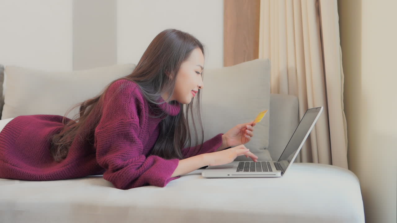 Happy Asian Female Shopaholic Shopping Online Using Laptop and Bank Credit Card From Confort of Her Living Room Couch, Full Frame
