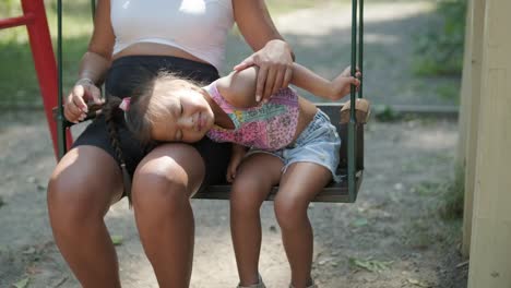 pregnant mother and daughter playing on swing outdoors