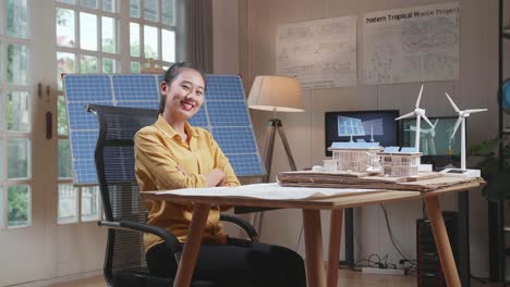 asian woman cross arms and smile to camera while working with a blueprint and the model small house with solar panel