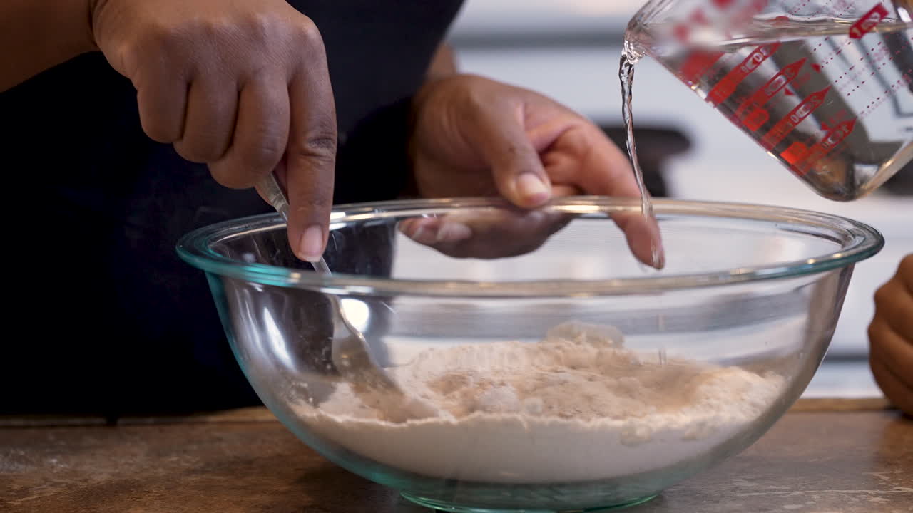 добавление воды к сухим ингредиентам для замешивания пасхального теста для пресного хлеба - замедленная съемка