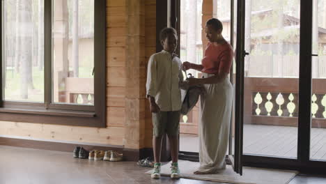 lovely mother helping his son to put on school bag in the patio at home, then hugging him and the boy leaving