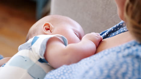 over the shoulder close up slow motion shot of mother sitting on sofa at home and breastfeeding baby