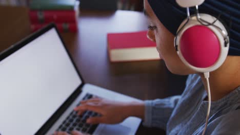 estudiante asiática vestida con un hijab azul sentada y escuchando música en la biblioteca