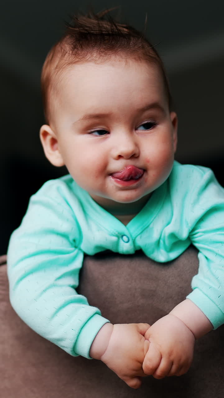 Playful beautiful kid with funny hair standing on the chair. Lovely toddler showing tongue and smiling. Low angle view. Vertical video