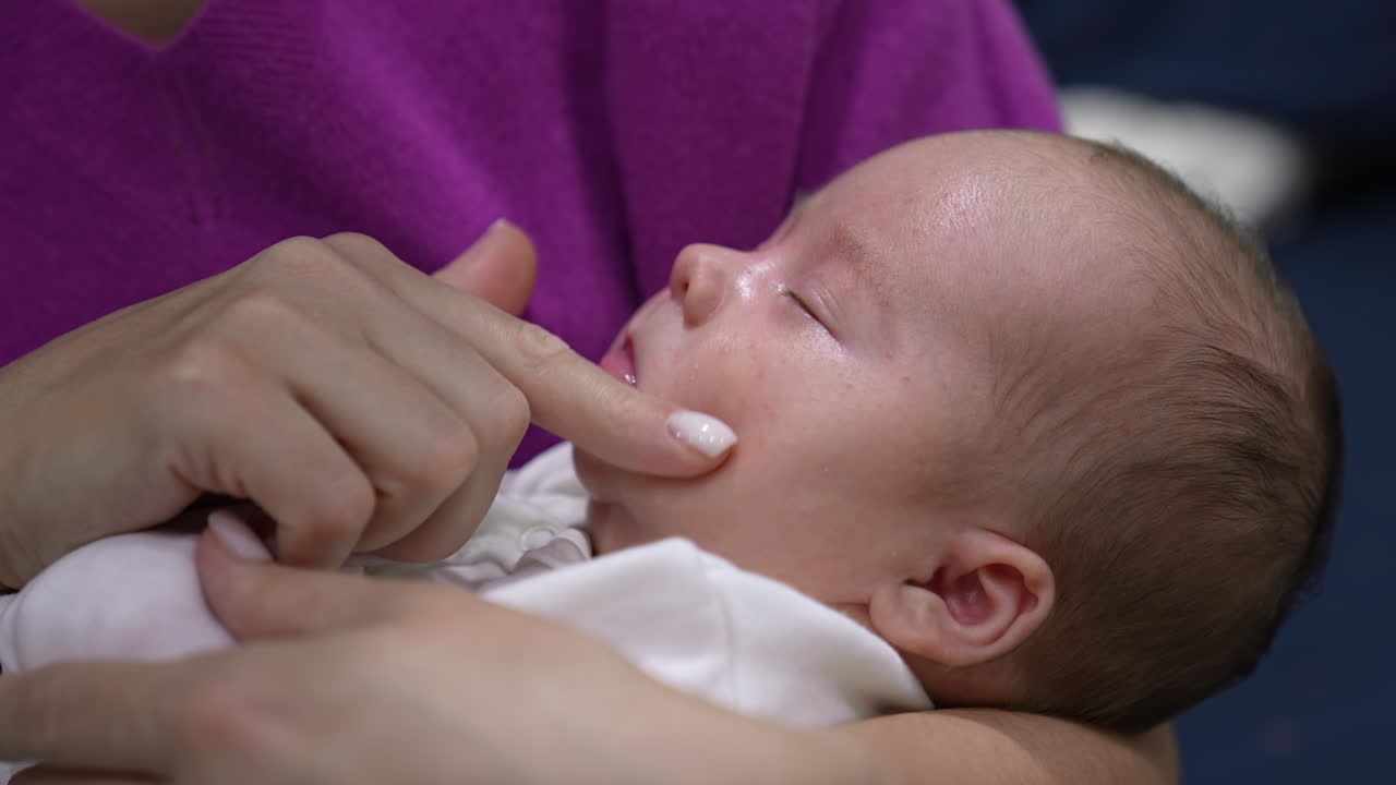 Beautiful infant in mother's embraces sleeps sweetly. Mother is trying to wake her son up by touching his chin, nose, cheeks. Cute boy doesn't want to wake up.