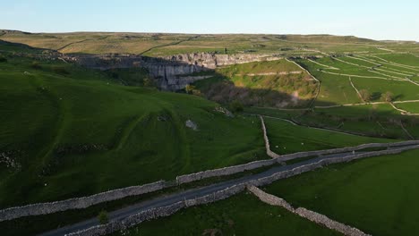 Rising-reveal-of-sun-setting-over-rocky-cliffside-gorge-as-shadow-moves-over-the-rocks-in-english-countryside-from-drone-at-Malham-Tarn-and-Gordale-Scar-Gorge
