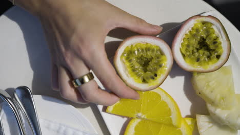 slow motion shot of a hand taking a half cut passionfruit from the plate