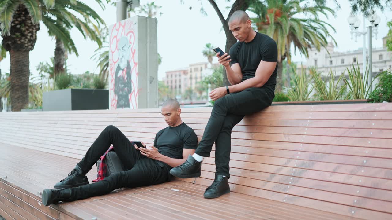 Two confident bald African brothers typing on phones