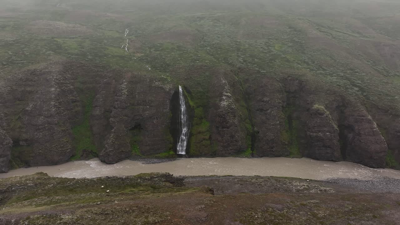 A moody drone view of Iceland’s Vesturdalur Hofsá River on a rainy day, with small waterfalls cascading into the valley and misty volcanic landscapes