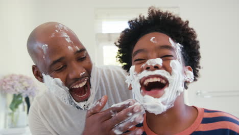 close up de padre e hijo en casa divirtiéndose jugando con espuma de afeitar en el baño haciendo un lío