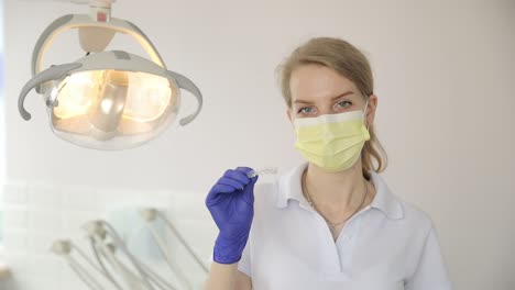a female dentist, with mask and gloves, holds a syringe while attending to a patient’s mouth.