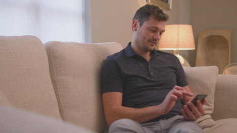 evening shot of man relaxing on sofa at home looking at mobile phone - shot in slow motion