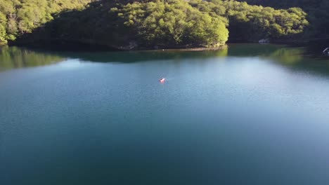 smooth drone orbit shot of a couple kayaking in beautiful quiet lake surrounded by outstanfing pine forest. in El Bolson, Argentina shot with DJI mini 3