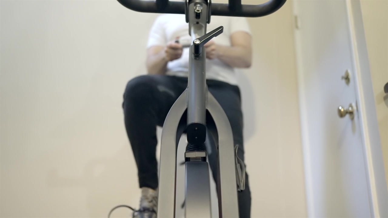 Atleta irreconocible haciendo ejercicio en bicicleta de spinning en un entorno doméstico.