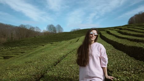 young woman raises her arms up against a background of tea bushes