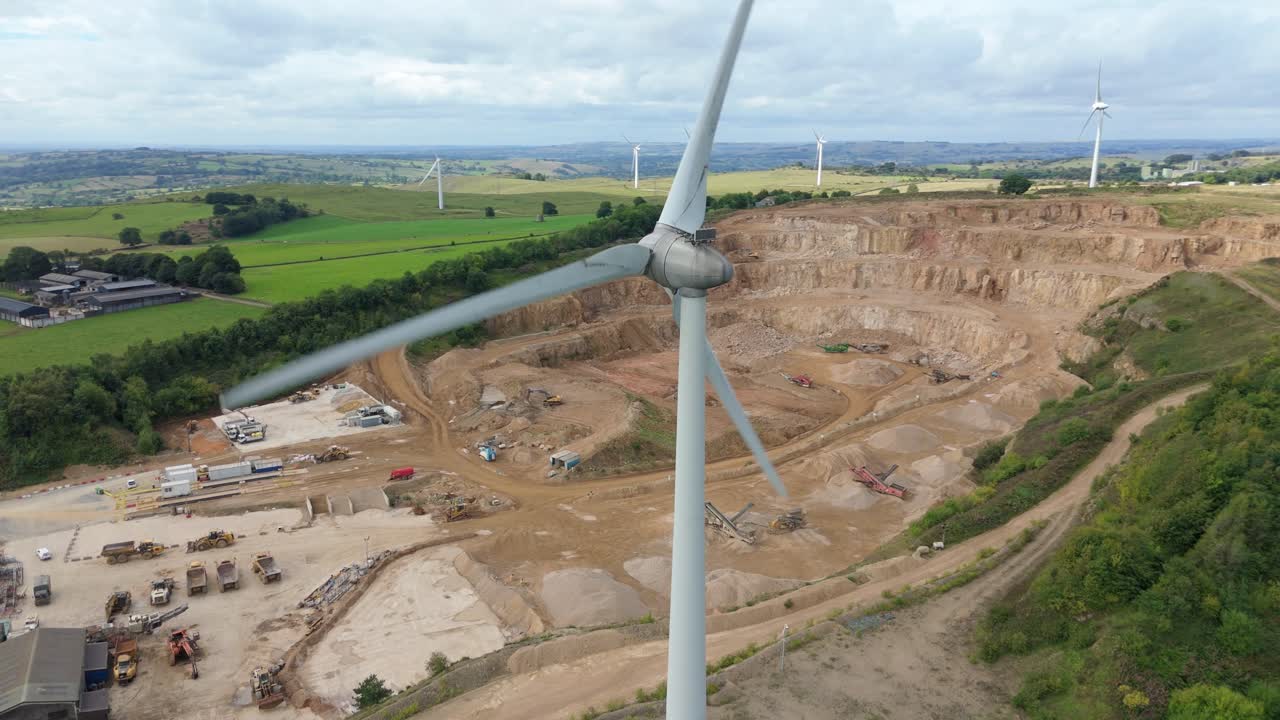 Aerial drone view of wind turbines generating electricity near quarry and factories in rural green landscape Derbyshire Dales United Kingdom