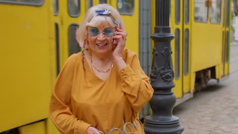 senior old tourist woman in stylish clothes talking on mobile phone while walking on city street