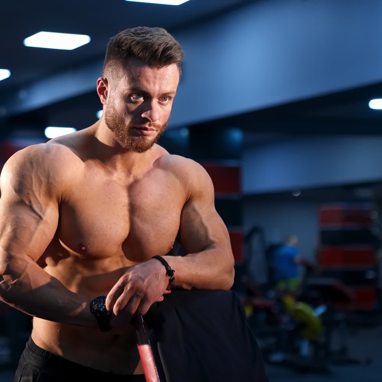 Muscular male athlete with naked torso in gym. Handsome bodybuilder with athletic body rests after hard training. Body care concept.